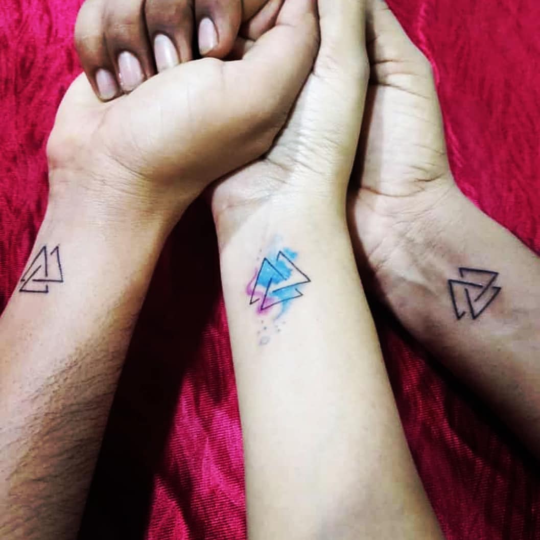 Three forearms with matching geometric arrow tattoos, one in color